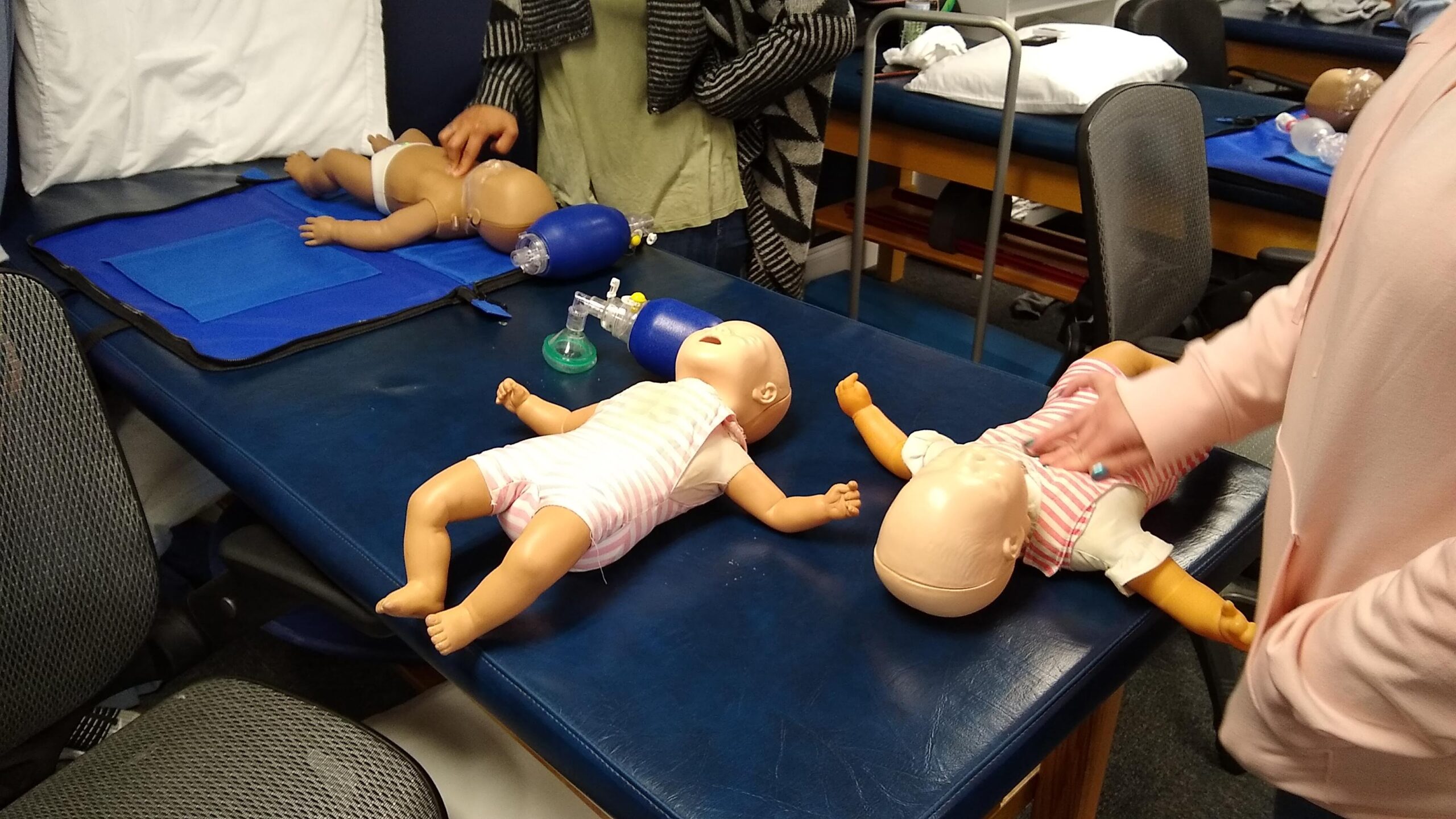 A diverse group of individuals collaboratively working on a baby doll, showcasing teamwork and creativity in their project_BLS certification Augusta_ACLS near me_ACLS classes near me_ACLS class near me