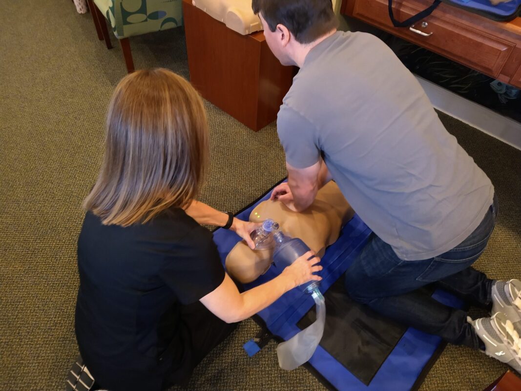 A man and woman perform emergency CPR on a man lying on the ground, demonstrating life-saving techniques_AHA CPR BLS Augusta