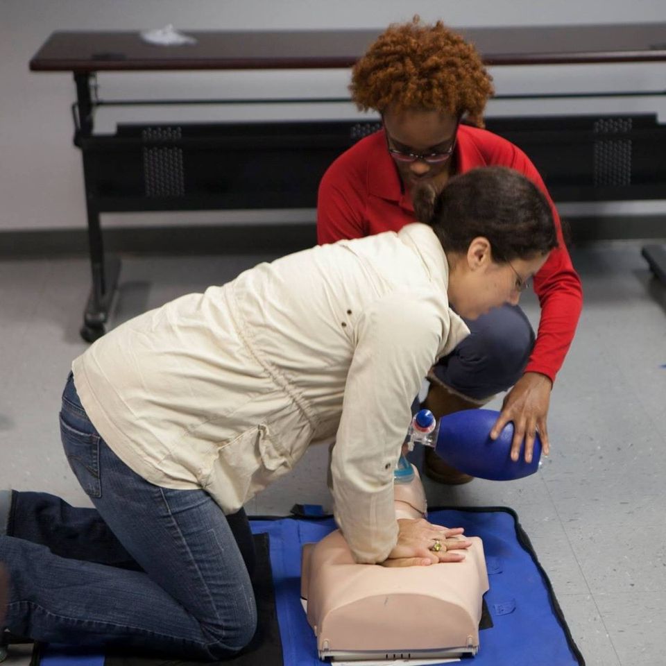 A woman assists another woman in using an AED, demonstrating emergency response skills in a critical situation_ACLS classes Augusta