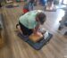 A woman performs an exercise on a mannequin, showcasing proper form and technique in a training environment.