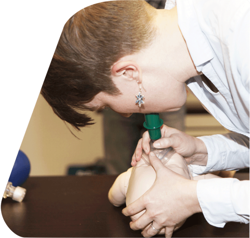 A woman is carefully placing a CPR mask over a mannequin's face, demonstrating proper resuscitation techniques.